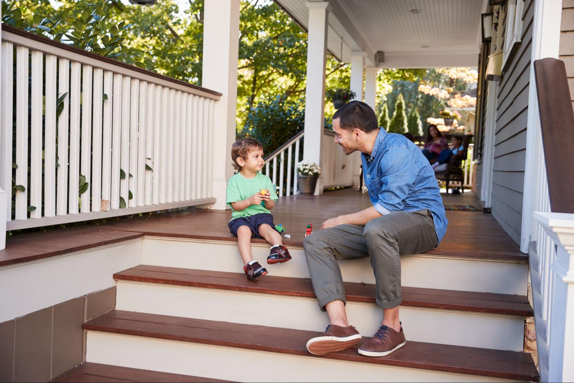 Father and son sit on the porch playing with toys, surrounded by sturdy vinyl railings for decks, creating a safe and stylish outdoor space.