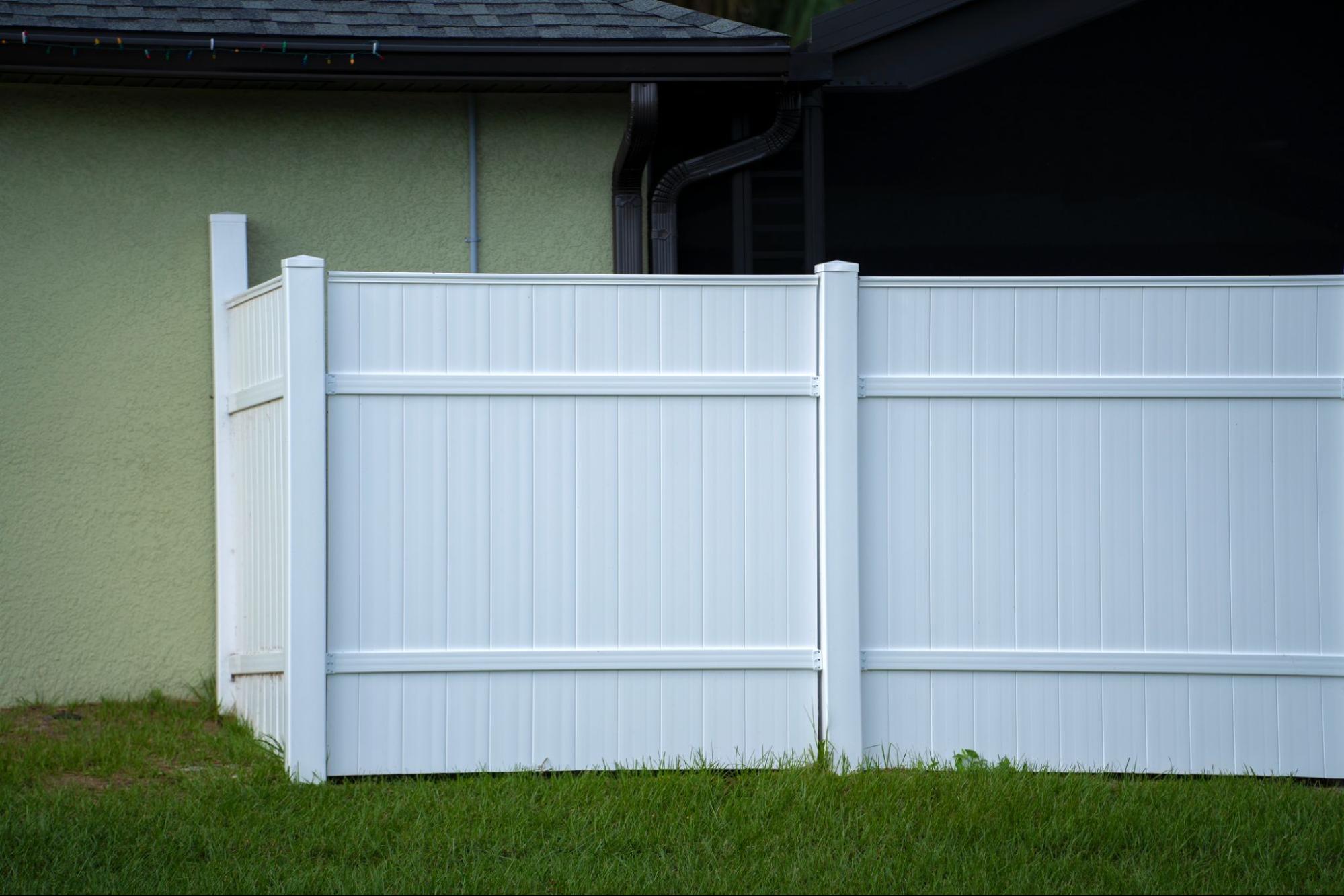 White vinyl picket fence at the back of a residential house.