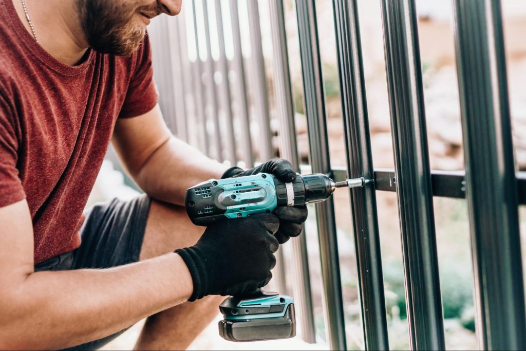 A male worker installs the gate fences with an electric screwdriver.