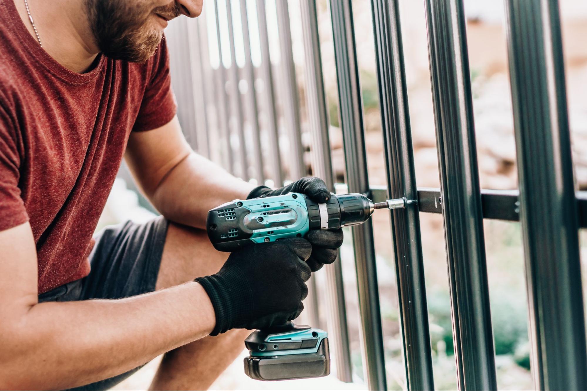 A male worker installs the gate fences with an electric screwdriver.