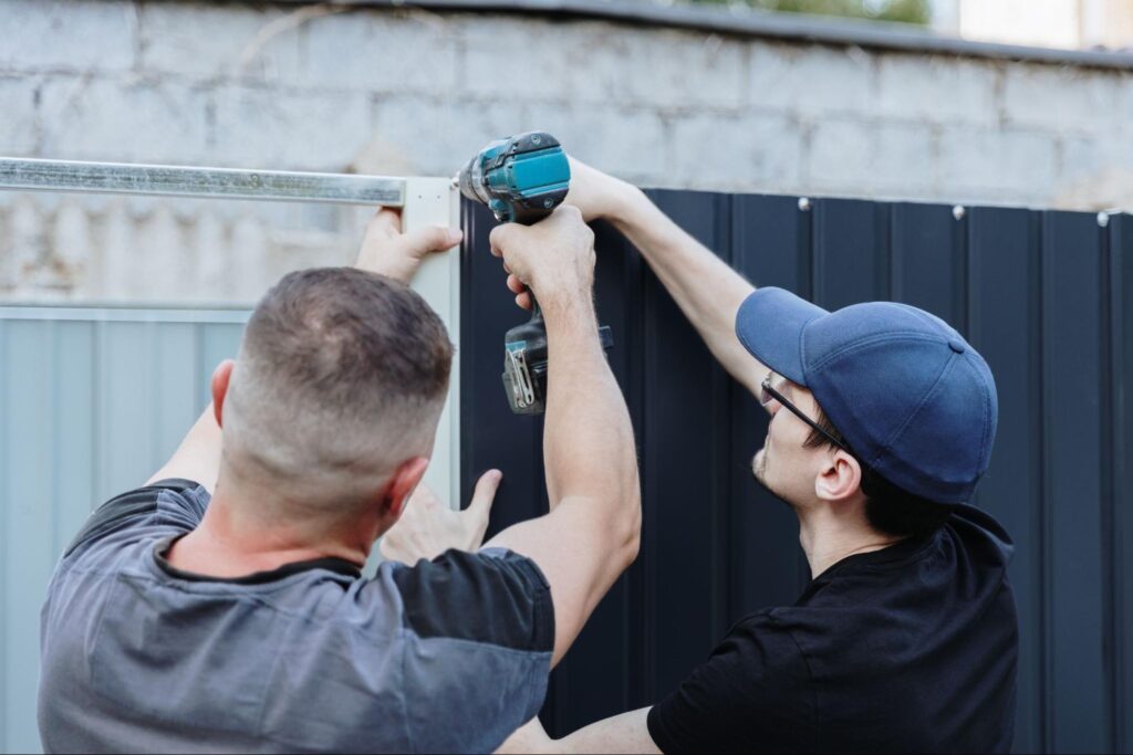 Rear view of installers using a drill to fasten screws into an aluminum fence panel