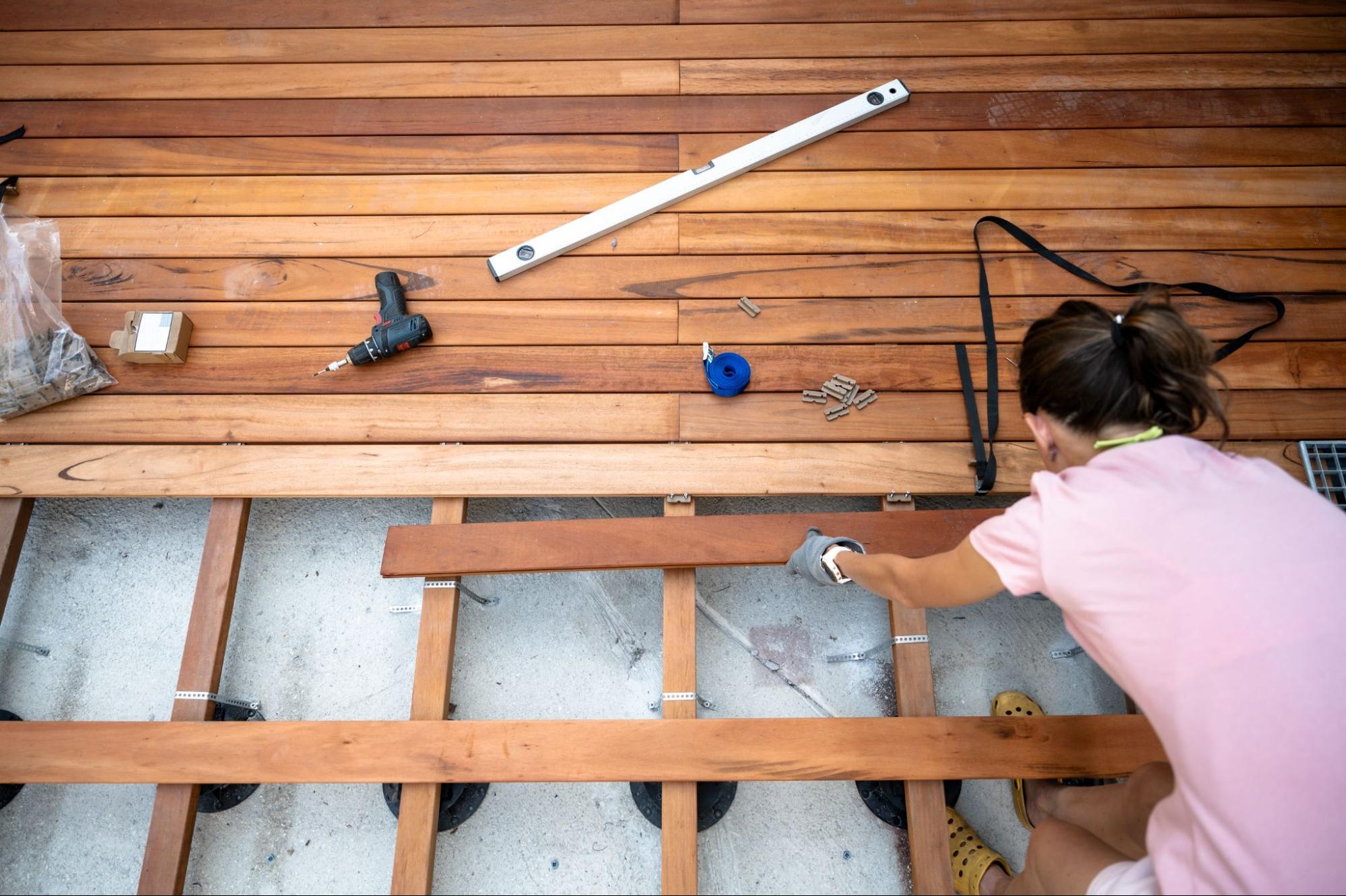 Top-down view of a woman assembling a wooden deck frame during construction.