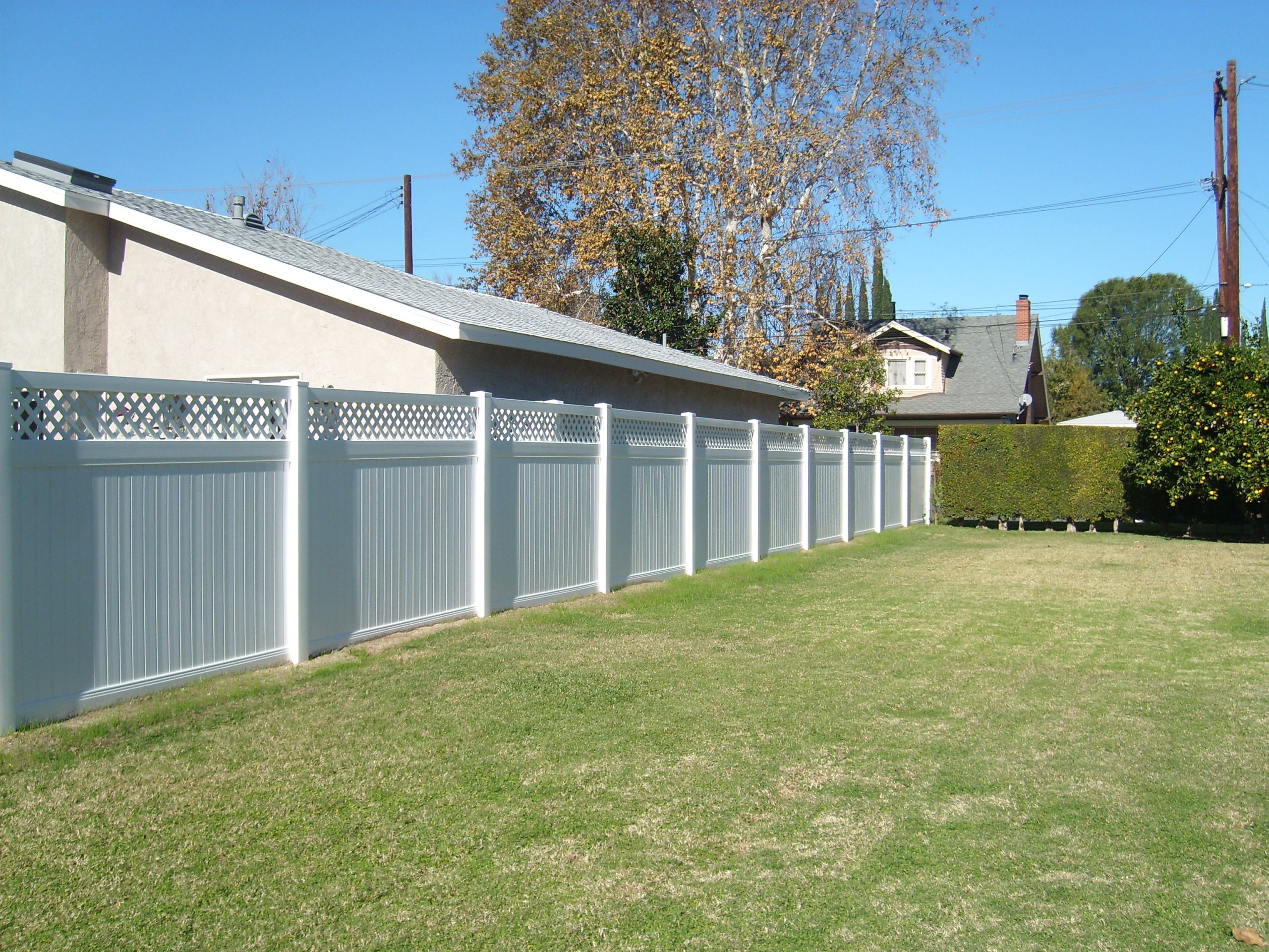 A close-up view of a white vinyl picket fence featuring a matching gate, set on a vibrant green lawn, enclosing a well-maintained property.